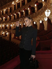 Woman in a black outfit standing in an ornate theater with red seats and gold accents.