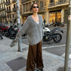 Woman in a gray cardigan and brown pants standing on a city street with parked motorcycles.