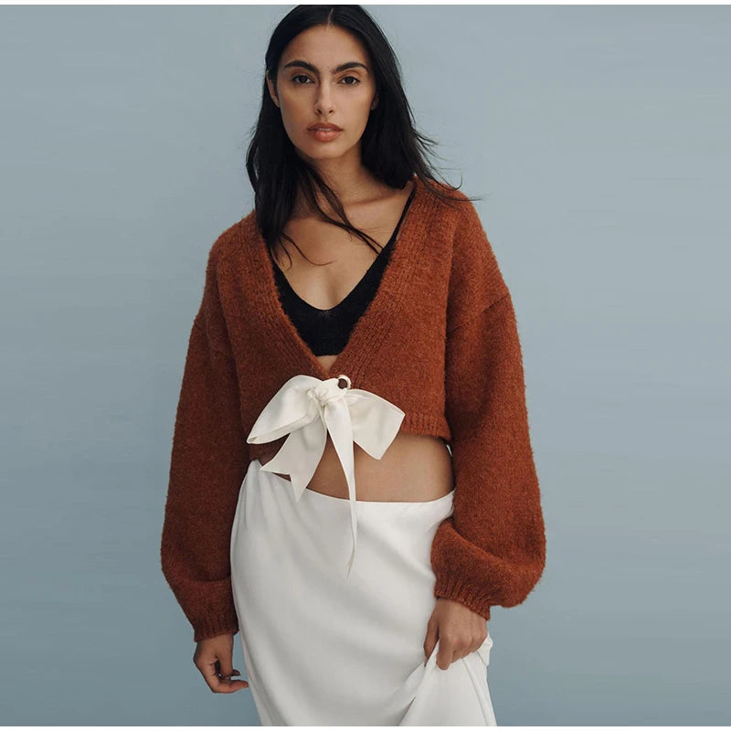 Woman wearing a brown cardigan over a black top and white skirt on a gray background