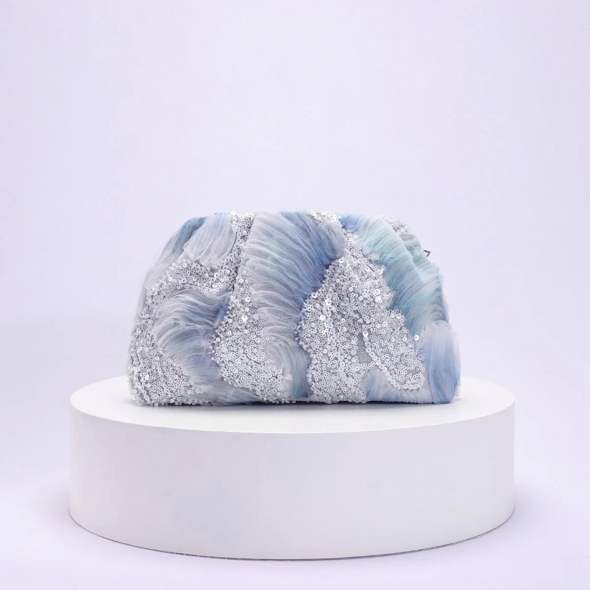 Blue and white marbled clutch with glittery accents on a white platform against a light purple background