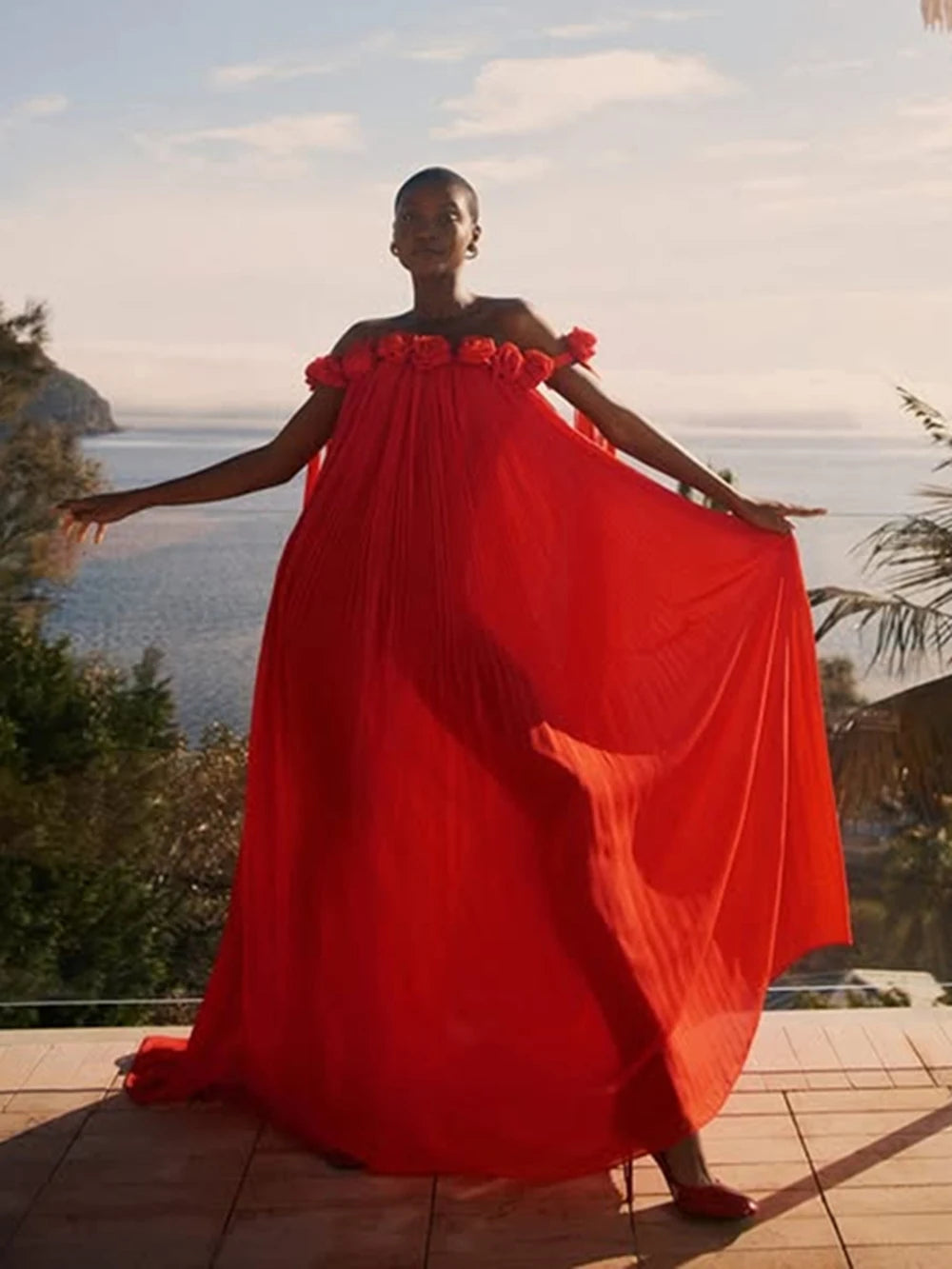 Model wearing a flowing red floral maxi dress by the sea