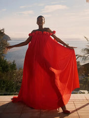 Model wearing a flowing red floral maxi dress by the sea