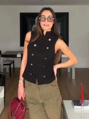 Woman wearing a black sleeveless jacket with gold buttons and green cargo pants indoors.