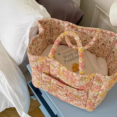 Floral-patterned fabric basket with a book titled 'Book of Pudding' on a bed.