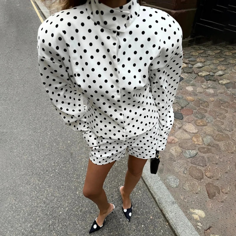 Person wearing a white dress with black polka dots on a street.