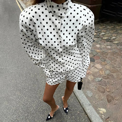 Person wearing a white dress with black polka dots on a street.