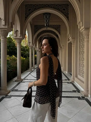Woman in a black polka dot top and white pants standing in an ornate colonnade.
