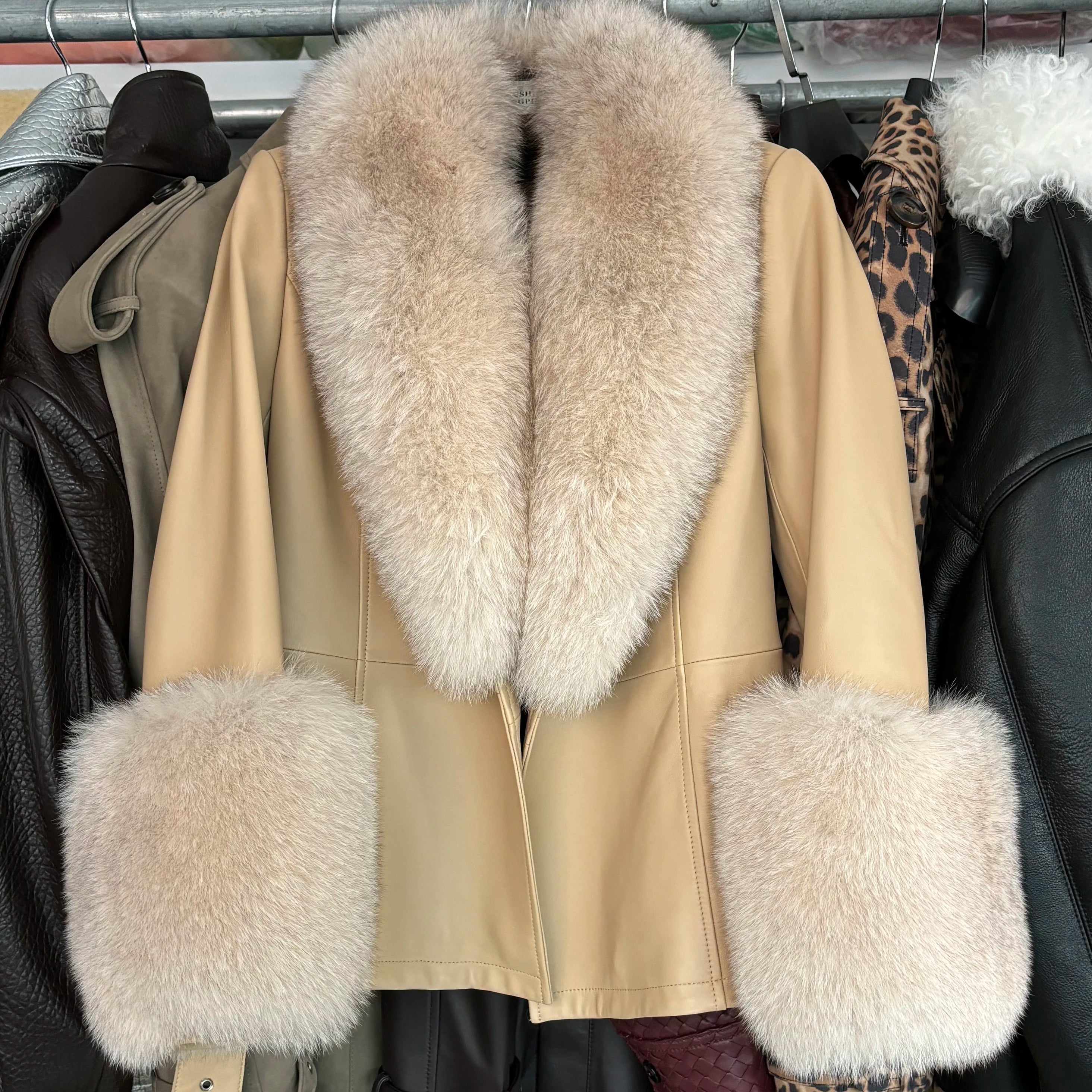 Beige coat with fur trim hanging on a rack among other coats.