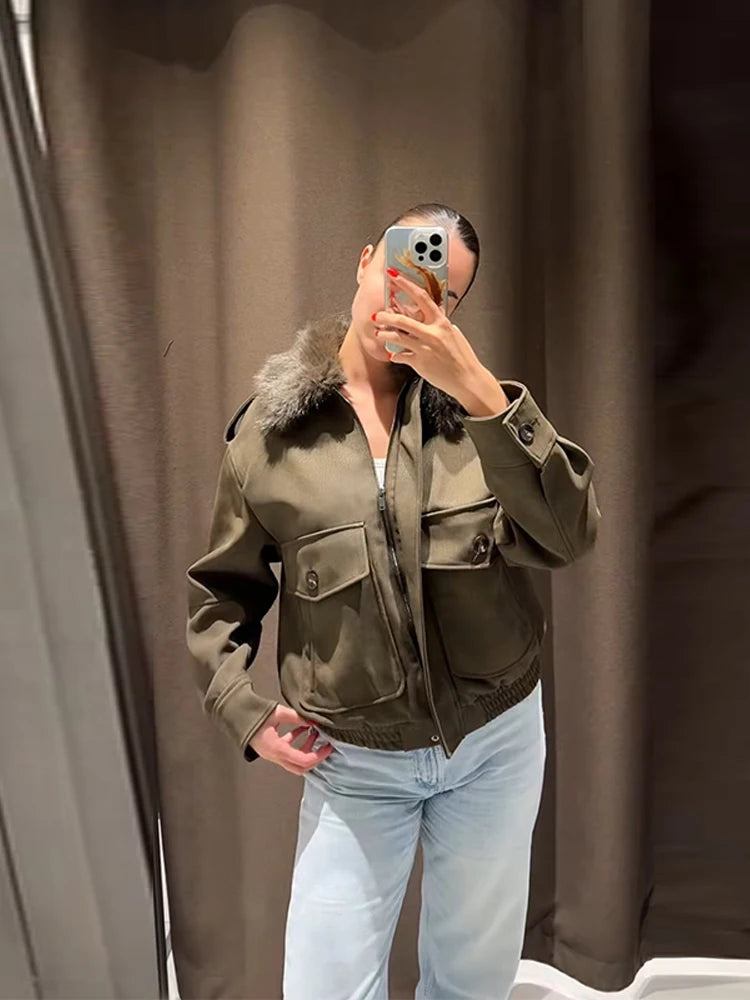 Person wearing a green jacket with fur collar taking a mirror selfie against a brown curtain.