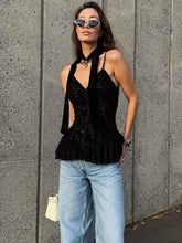 Woman wearing a black peplum top and blue jeans against a gray wall.