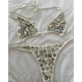 White embellished bikini set laying flat on a white textured surface.