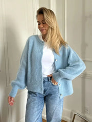 Woman wearing a light blue cardigan over a white shirt and blue jeans indoors.