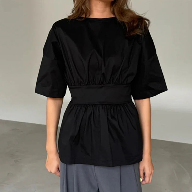 Person wearing a black top with puffed sleeves and a plain background