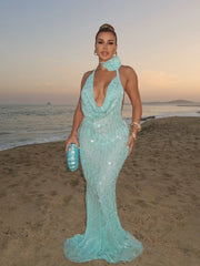 Woman in a light blue evening gown standing on a beach at sunset.