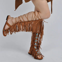 Close-up of model's legs wearing brown embellished lace-up fringe gladiator sandals