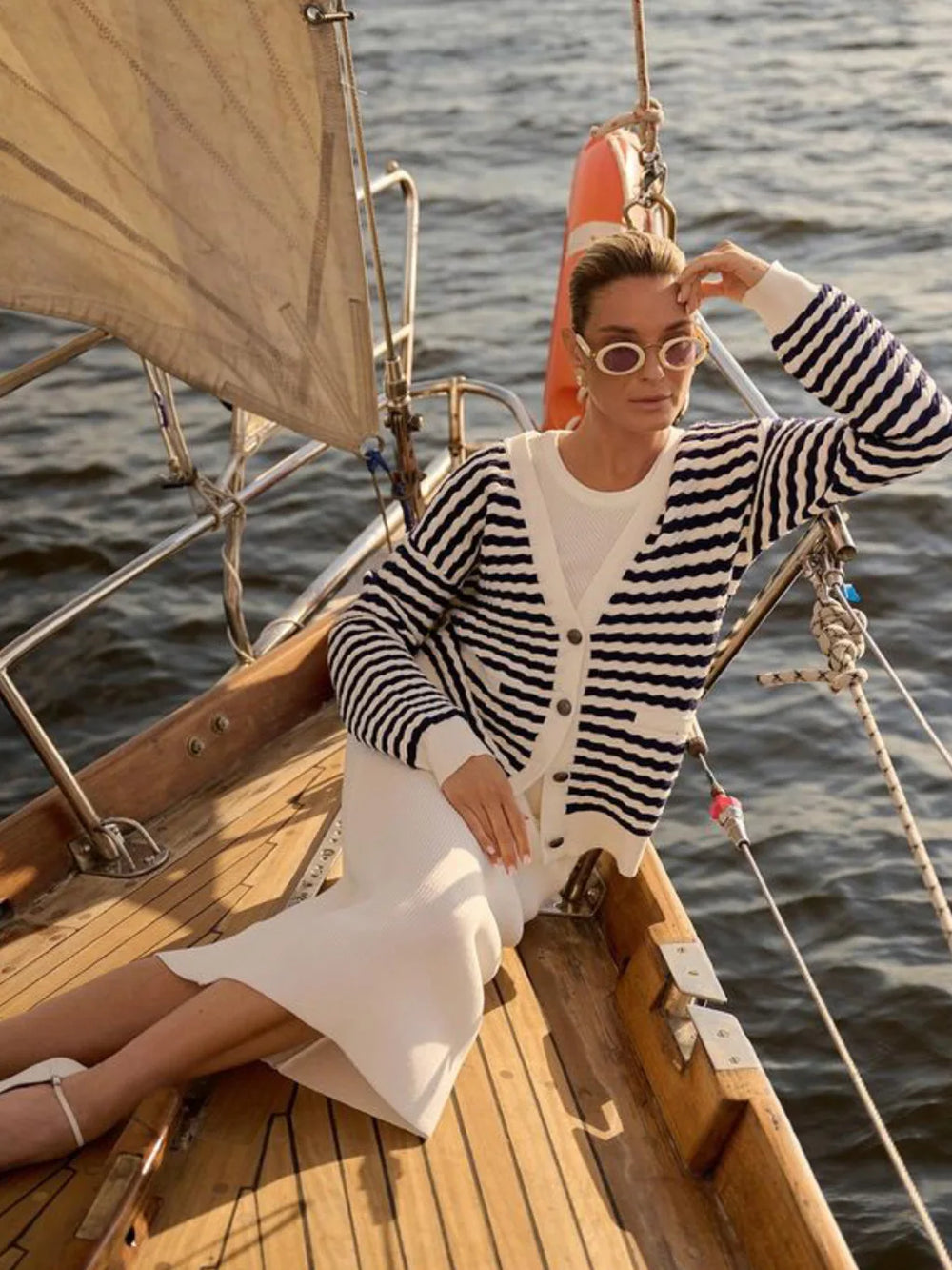 Woman on a sailboat wearing a striped sweater and sunglasses with water in the background