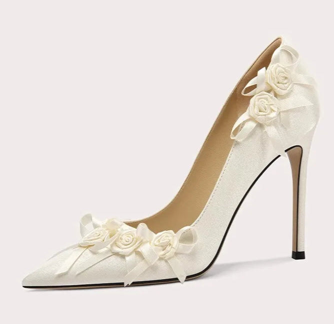 White high-heeled shoe with floral decorations on a light gray background