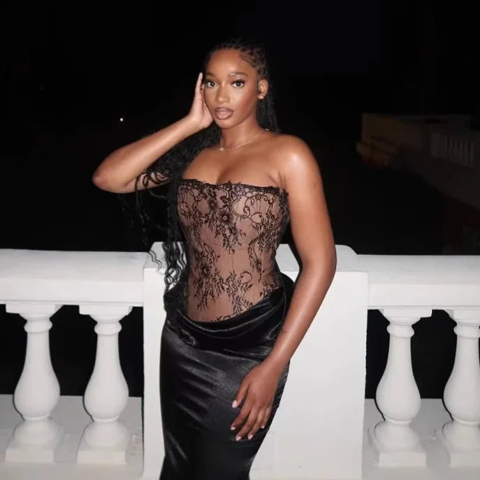 Woman wearing a black lace top and black skirt on a white railing at night.