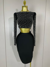 Black dress set with pearl embellishments on a mannequin against a white background