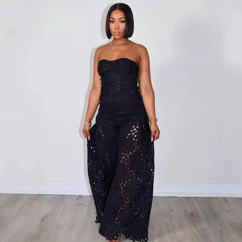 Woman wearing a black strapless jumpsuit with cut-out details against a white wall.