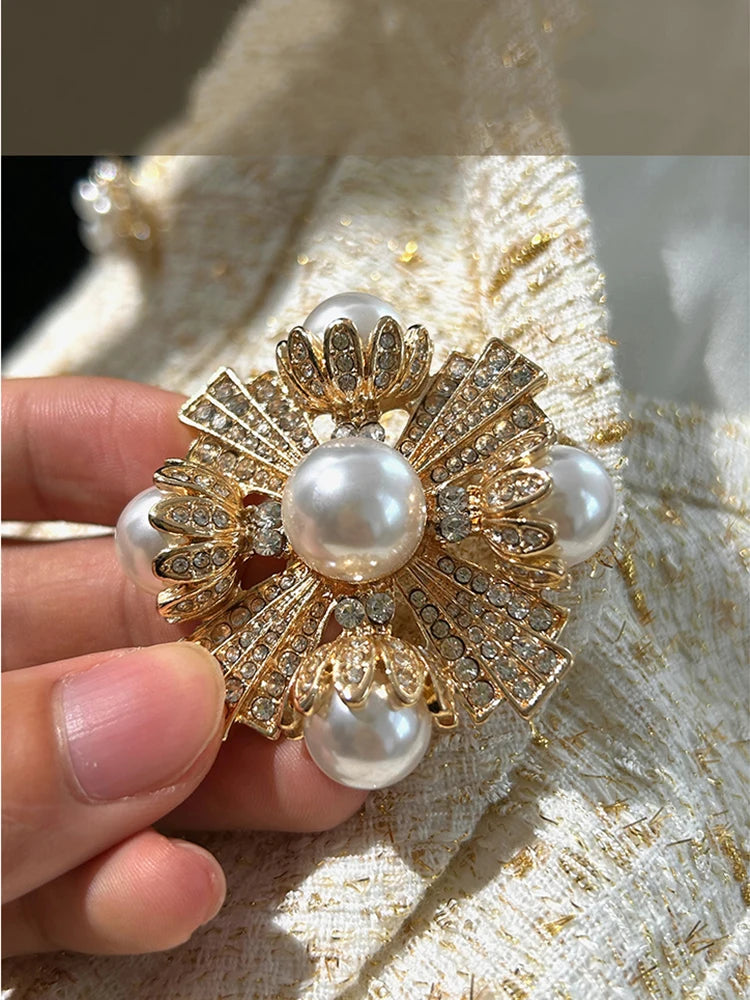 Gold brooch with pearls held by a hand against a textured beige background