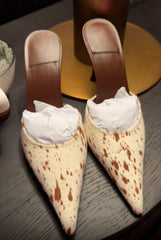 Close-up of two cow print stiletto heels with tissue stuffing