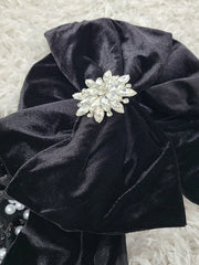 Black satin headband with a decorative pearl flower on a textured white background
