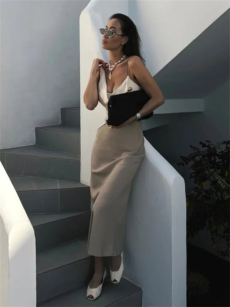 Woman in a beige dress standing on a staircase with a white wall and black steps.