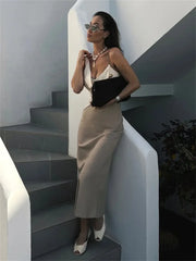 Woman in a beige dress standing on a staircase with a white wall and black steps.