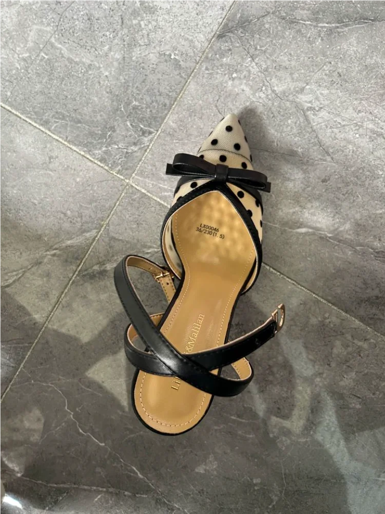 Black sandal with a bow on a gray tiled floor