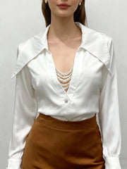 Woman wearing a white blouse with a deep neckline and brown skirt against a plain background