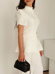 Person wearing a white outfit holding a black handbag against a plain background