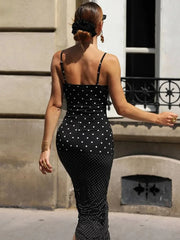 Woman wearing a black polka dot dress standing against a building.