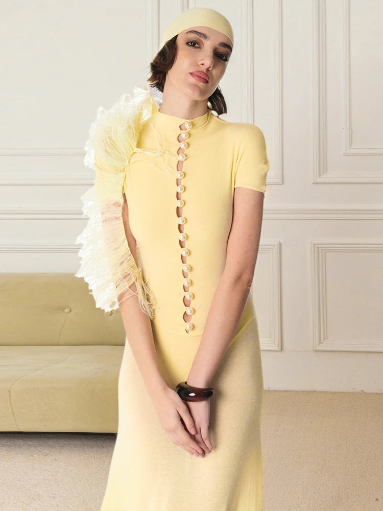Woman wearing a yellow dress with decorative buttons and ruffled sleeves in an elegant room.
