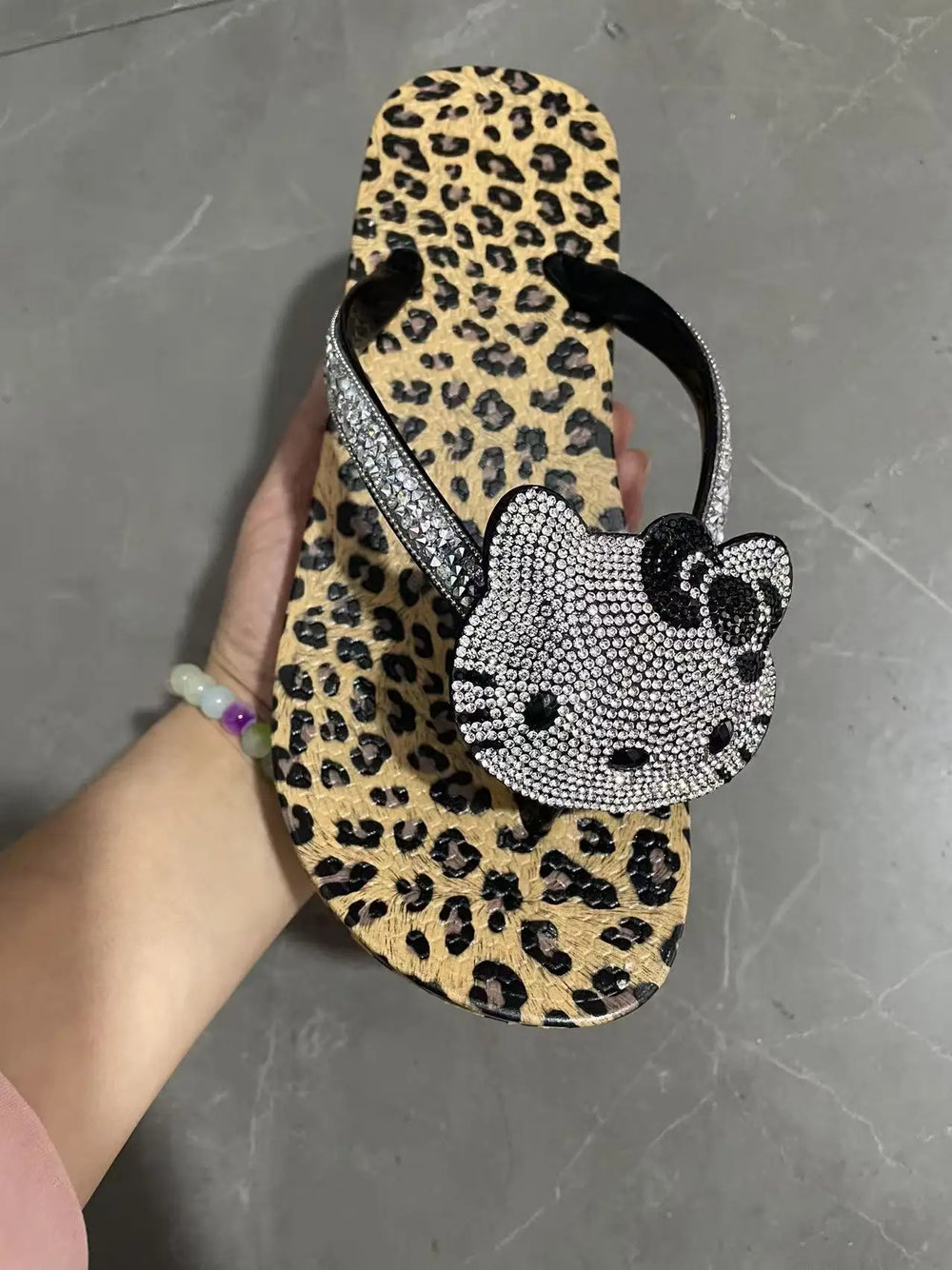 Hand holding a leopard print flip flop with a black bow and Hello Kitty rhinestone design