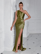 Woman wearing a green one-shoulder dress with a high slit in a white room.