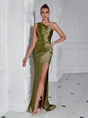 Woman wearing a green one-shoulder dress with a high slit in a white room.