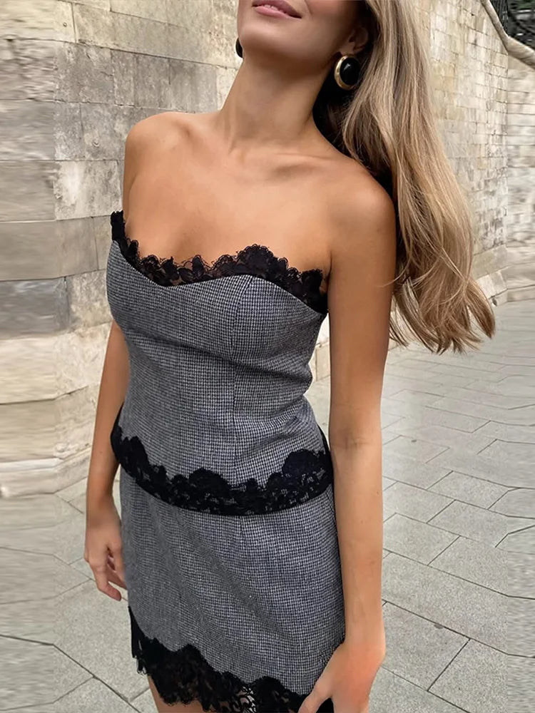 Woman wearing a strapless dress with black lace details against a stone wall background