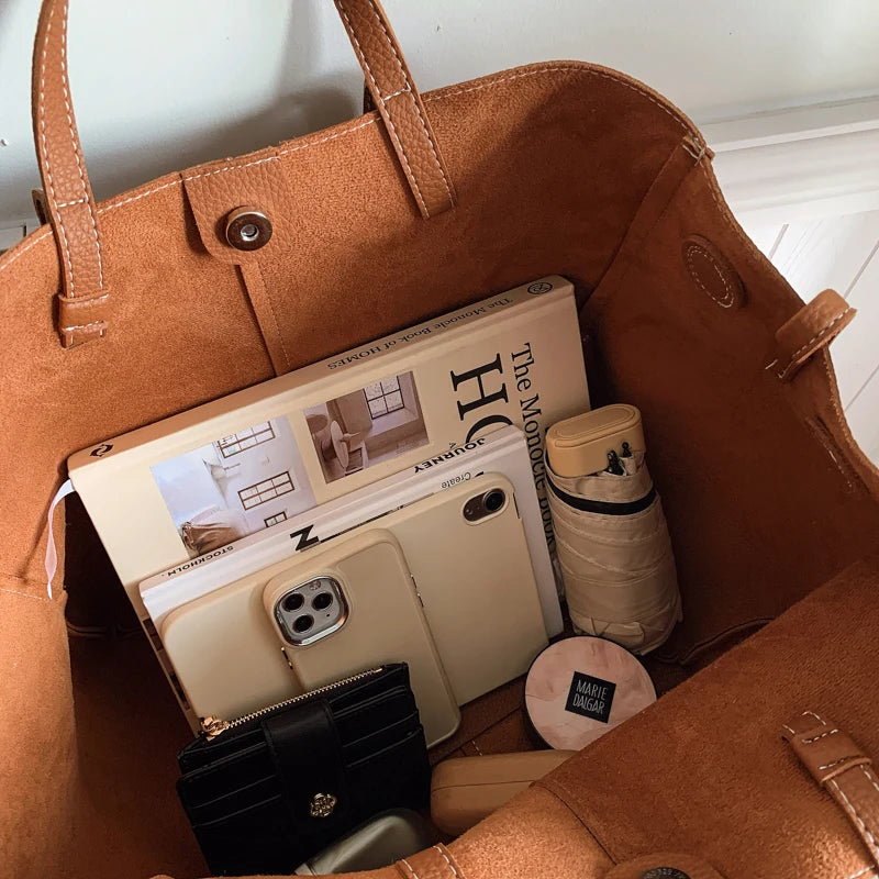 Brown handbag with items including a phone, magazine, and cylindrical container.
