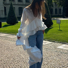 Person wearing a white ruffled blouse and blue jeans walking on a cobblestone path.