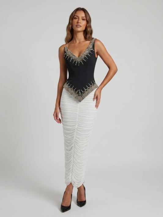 Model wearing a black beaded V-neck sleeveless top and a white ruched floor-length skirt.
