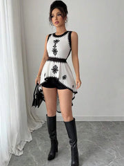 Woman wearing a white dress with black floral patterns and black knee-high boots in a minimalistic setting.