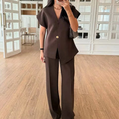 Person wearing a brown outfit with a gold button in a room with wooden flooring and white walls.