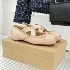 Beige ballet flats on a beige box with a black handbag and blue textured fabric in the background.