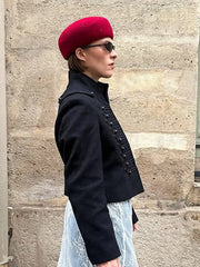 Person wearing a black coat, red beret, and sunglasses against a stone wall.