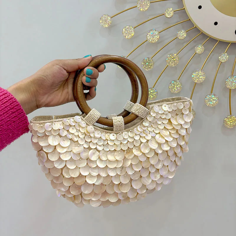 Hand holding a beaded handbag with wooden handle against a decorative wall.
