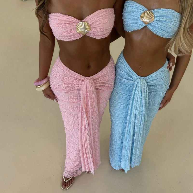 Two women wearing pink and blue sarongs with shell details on a beige background