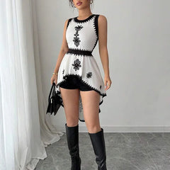 Woman wearing a white dress with black floral patterns and black knee-high boots in a minimalistic setting.