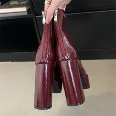 Burgundy high-heeled shoes held by a hand on a neutral background