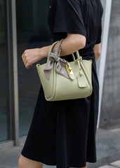 Person holding a light green handbag with a bow detail against a blurred background